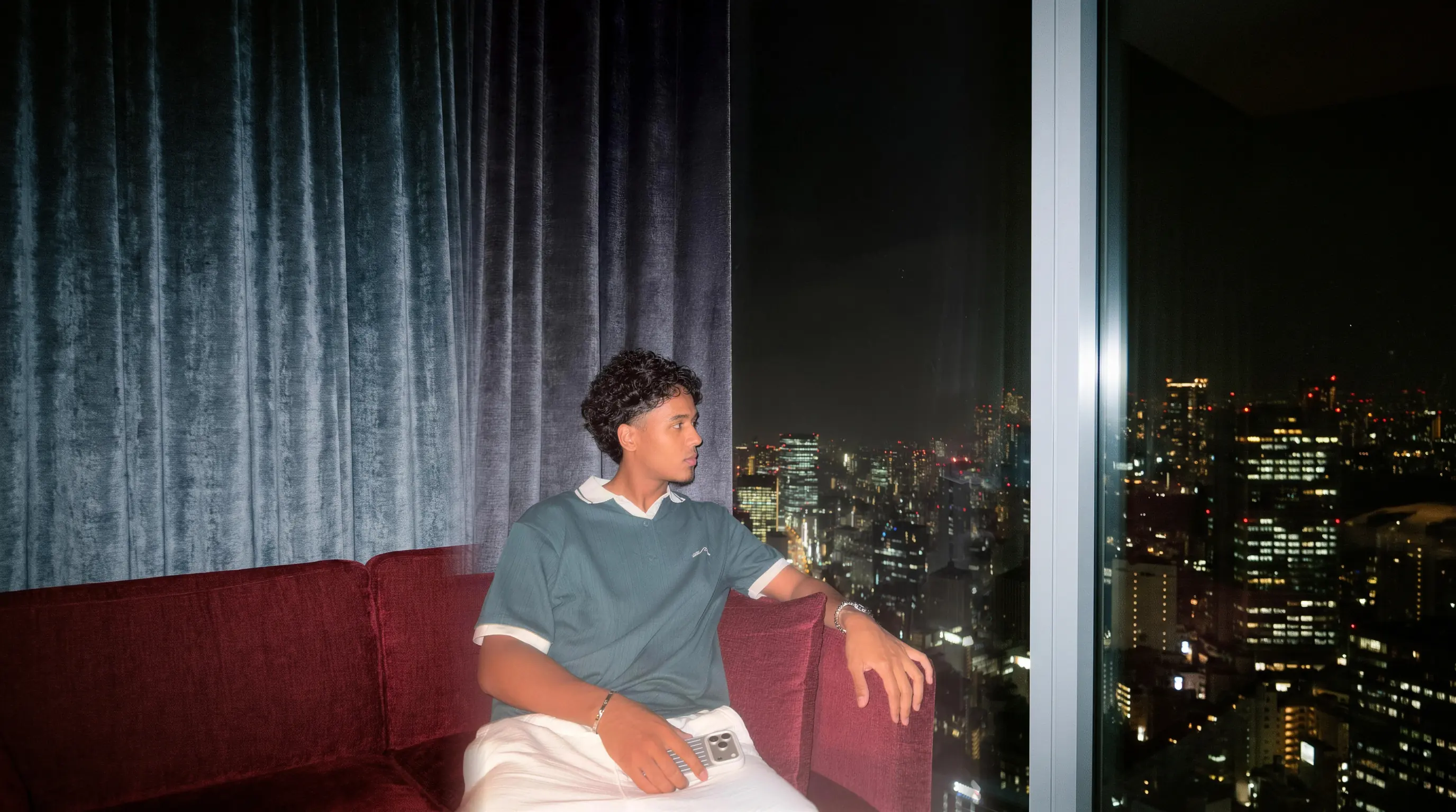 Amir Mohamed sitting on a sofa by a window above the city at night